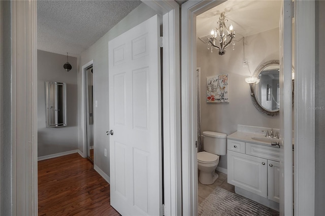 bathroom with vanity, a textured ceiling, hardwood / wood-style flooring, a chandelier, and toilet