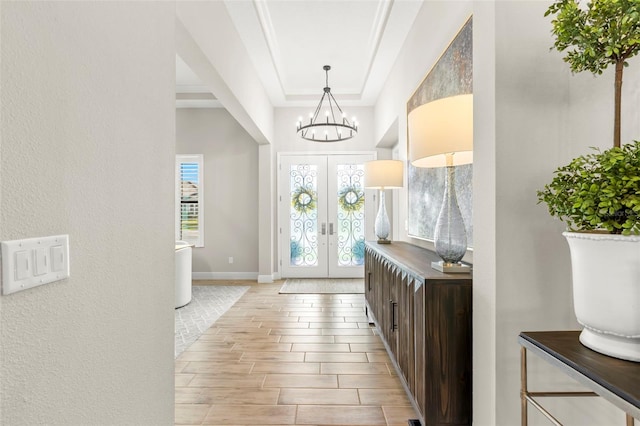 entrance foyer with a tray ceiling, a chandelier, light hardwood / wood-style flooring, crown molding, and french doors