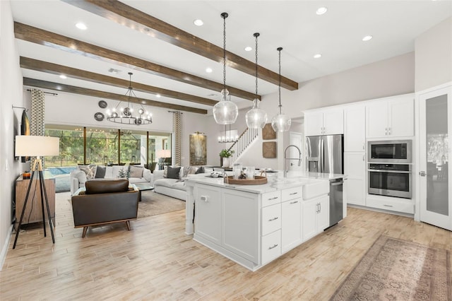 kitchen featuring a center island with sink, white cabinetry, appliances with stainless steel finishes, beam ceiling, and pendant lighting