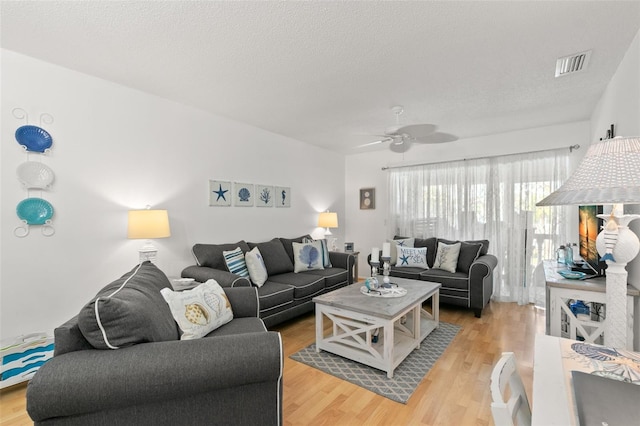 living room featuring ceiling fan, light hardwood / wood-style flooring, and a textured ceiling