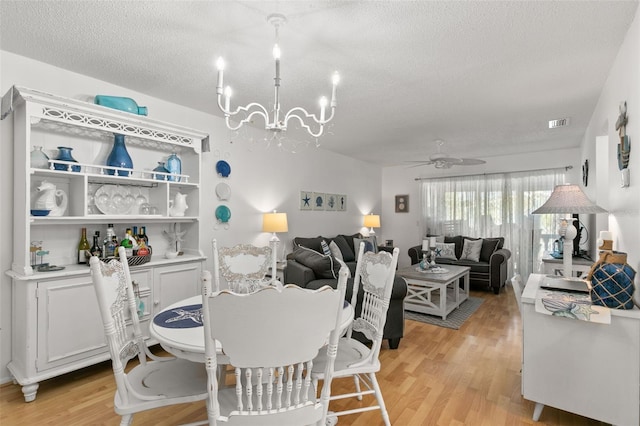 dining area with a textured ceiling, ceiling fan with notable chandelier, and light hardwood / wood-style flooring