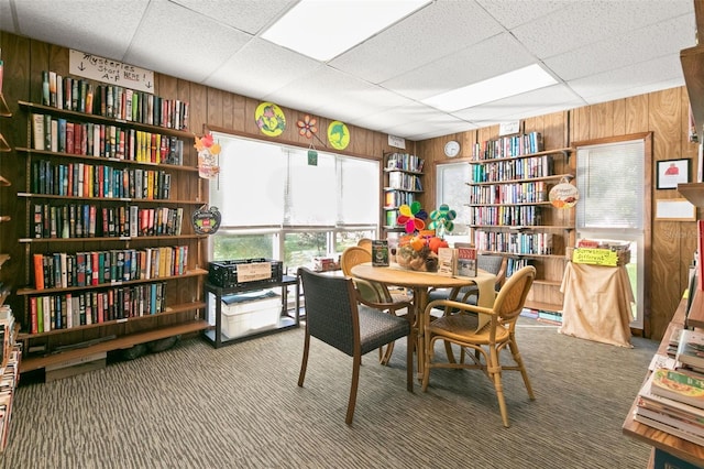 dining space with a drop ceiling, carpet floors, and wooden walls