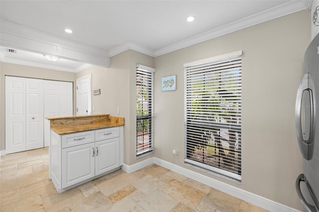 kitchen featuring white cabinetry, stainless steel refrigerator, light stone countertops, and crown molding