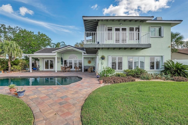 back of property featuring a lawn, a balcony, french doors, and a patio area