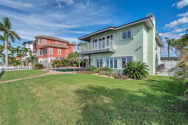 back of property featuring a lawn, a balcony, and a fenced in pool