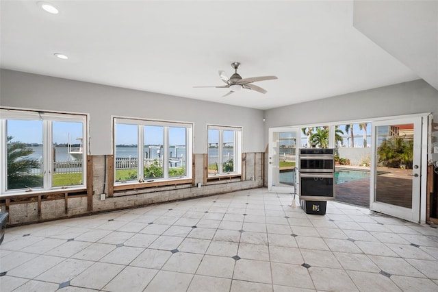 unfurnished sunroom featuring ceiling fan, a water view, and a healthy amount of sunlight