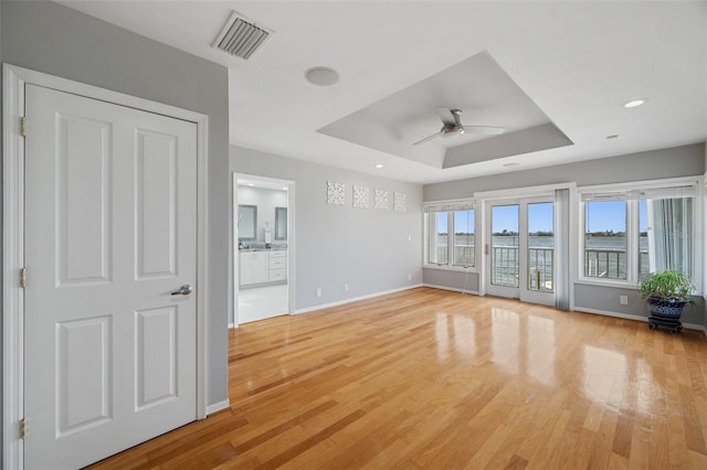 unfurnished living room with light wood-type flooring, ceiling fan, and a tray ceiling