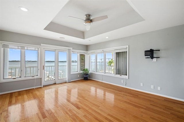 empty room with light hardwood / wood-style floors, ceiling fan, a raised ceiling, and a water view