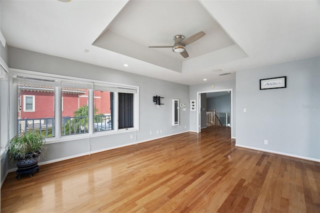 unfurnished living room with wood-type flooring, ceiling fan, and a raised ceiling