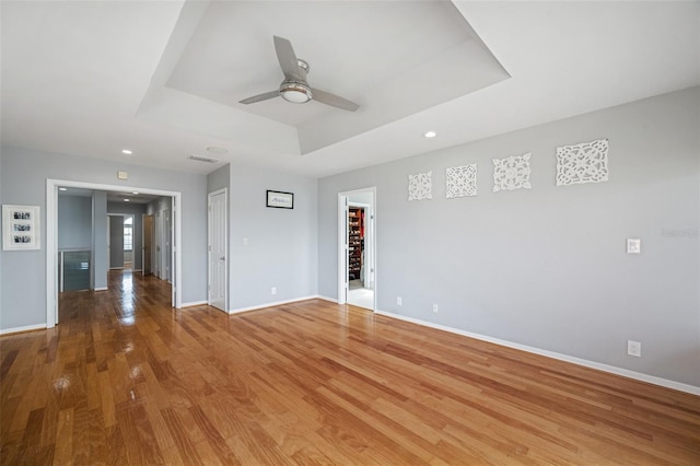 empty room featuring hardwood / wood-style floors, ceiling fan, and a raised ceiling