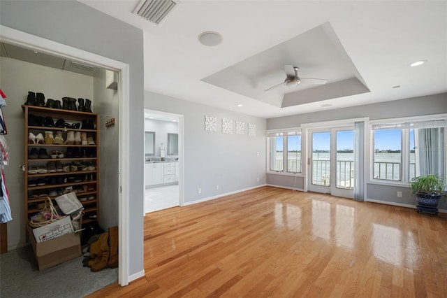 unfurnished living room with ceiling fan, a raised ceiling, and light hardwood / wood-style flooring