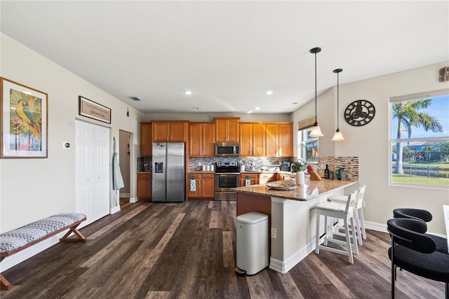 kitchen with kitchen peninsula, decorative light fixtures, stainless steel appliances, and a wealth of natural light