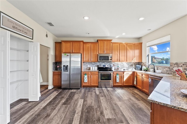 kitchen with appliances with stainless steel finishes, backsplash, light stone counters, dark wood-type flooring, and sink