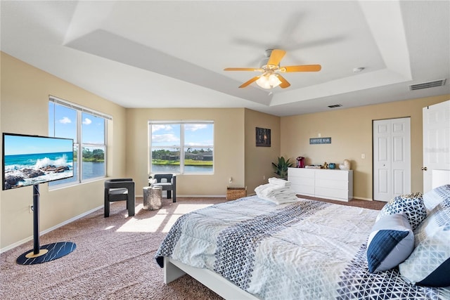 bedroom with a tray ceiling, ceiling fan, light colored carpet, and a water view