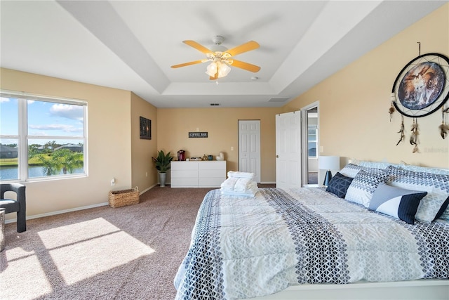 bedroom with ceiling fan, a water view, carpet floors, and a tray ceiling