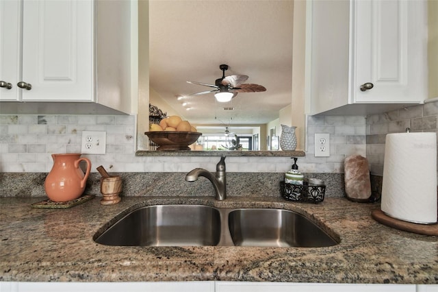 kitchen with dark stone counters, white cabinets, sink, decorative backsplash, and ceiling fan