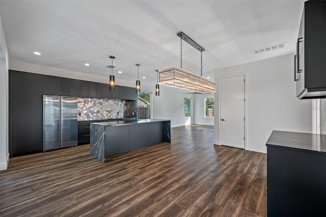 kitchen with stainless steel refrigerator, sink, dark hardwood / wood-style flooring, an island with sink, and decorative light fixtures