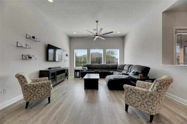 living room with ceiling fan, light wood-type flooring, and a textured ceiling