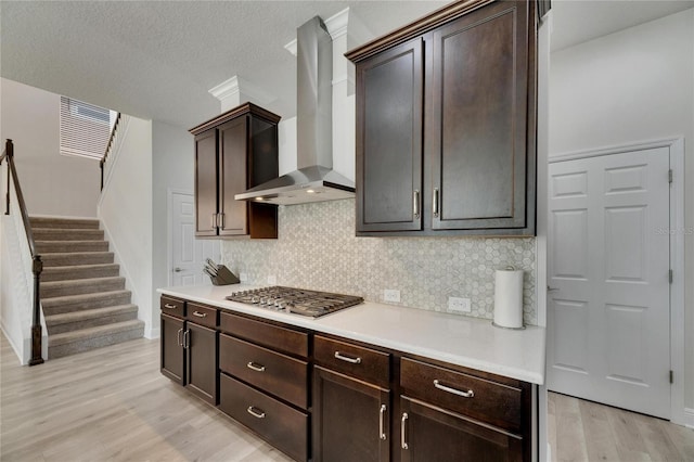 kitchen with stainless steel gas stovetop, wall chimney range hood, light hardwood / wood-style flooring, tasteful backsplash, and dark brown cabinetry