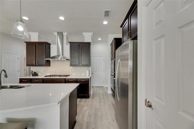 kitchen featuring sink, wall chimney exhaust hood, decorative light fixtures, light hardwood / wood-style floors, and stainless steel appliances