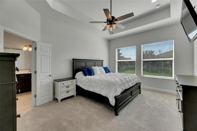 carpeted bedroom featuring a tray ceiling, ensuite bathroom, and ceiling fan