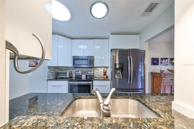 kitchen featuring white cabinetry, stainless steel appliances, dark stone counters, and sink