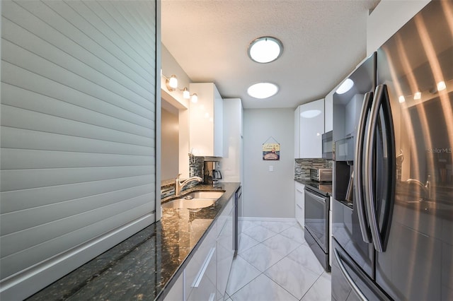 kitchen with white cabinets, appliances with stainless steel finishes, dark stone counters, and sink