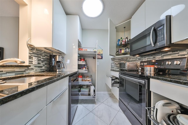 kitchen with white cabinetry, stainless steel appliances, light tile patterned floors, and backsplash