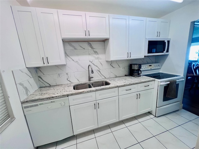 kitchen with tasteful backsplash, light stone counters, white appliances, sink, and white cabinetry