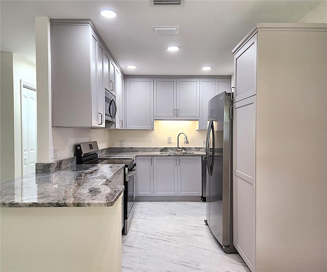 kitchen featuring sink, stainless steel appliances, kitchen peninsula, dark stone countertops, and gray cabinets