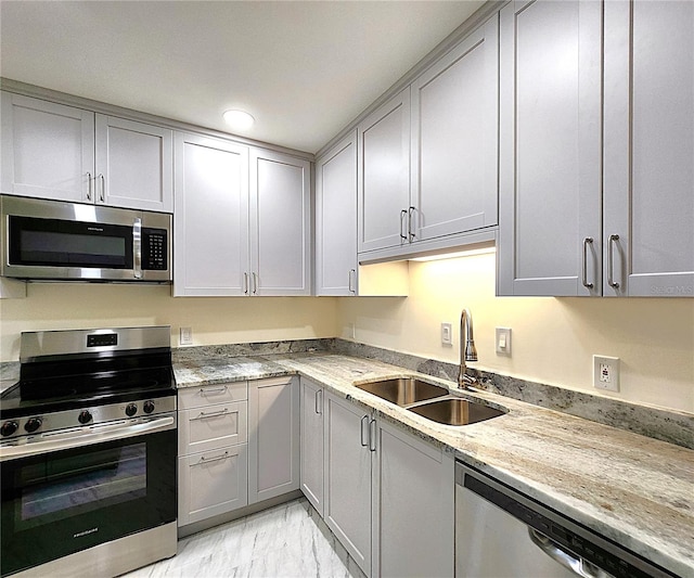 kitchen with gray cabinets, light stone counters, sink, and stainless steel appliances