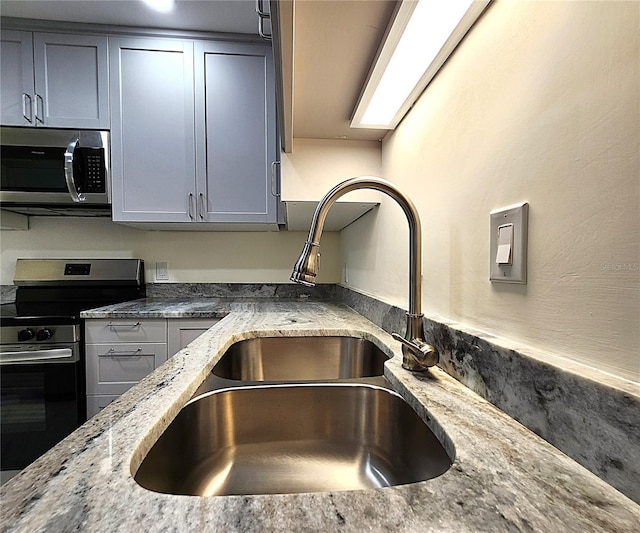 kitchen with gray cabinets, light stone counters, sink, and appliances with stainless steel finishes