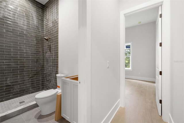 bathroom with hardwood / wood-style flooring, toilet, and a tile shower