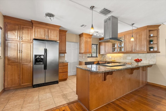 kitchen with pendant lighting, stainless steel refrigerator with ice dispenser, dark stone countertops, light hardwood / wood-style floors, and island range hood