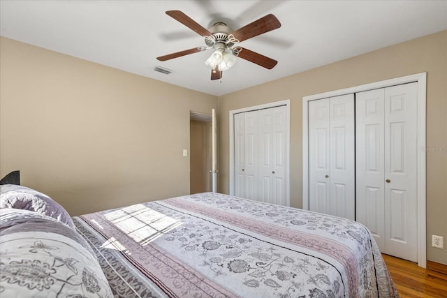 bedroom with ceiling fan, two closets, and hardwood / wood-style flooring