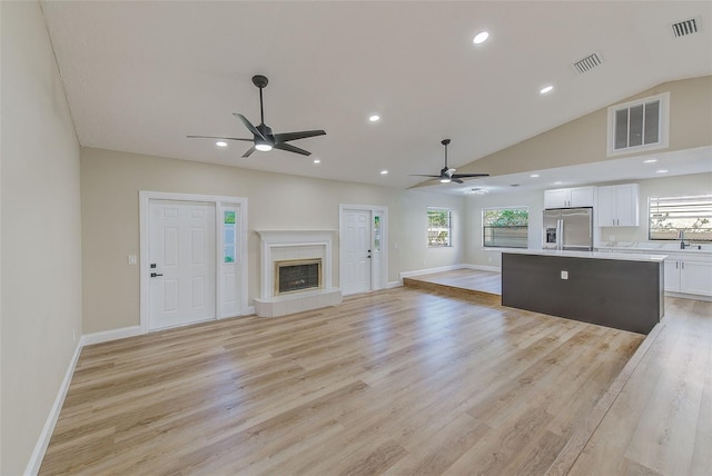 unfurnished living room with sink, lofted ceiling, light wood-type flooring, ceiling fan, and a tile fireplace