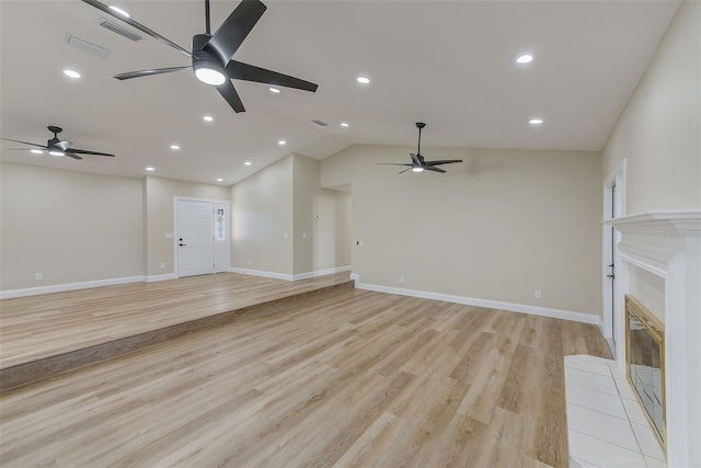 unfurnished living room featuring light hardwood / wood-style flooring, vaulted ceiling, and a tiled fireplace