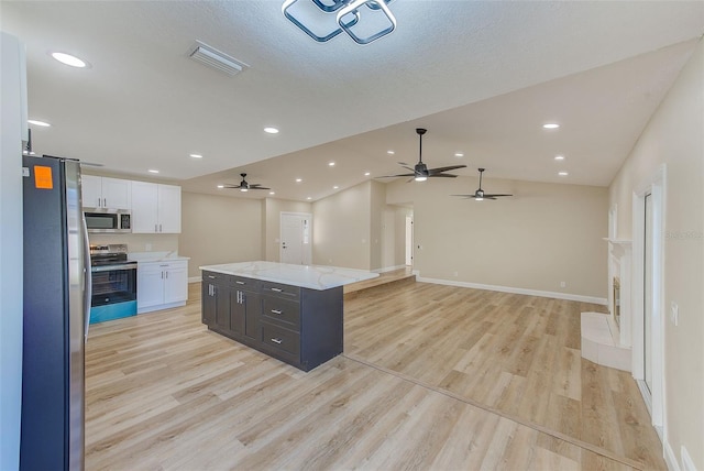 kitchen with white cabinetry, vaulted ceiling, appliances with stainless steel finishes, a center island, and light wood-type flooring