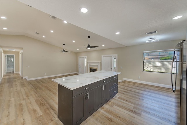 kitchen featuring light hardwood / wood-style flooring, ceiling fan, vaulted ceiling, stainless steel refrigerator, and light stone countertops