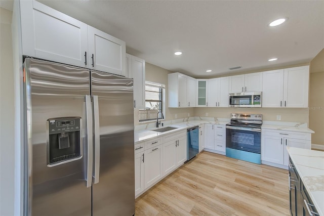 kitchen with appliances with stainless steel finishes, light hardwood / wood-style floors, white cabinetry, and sink