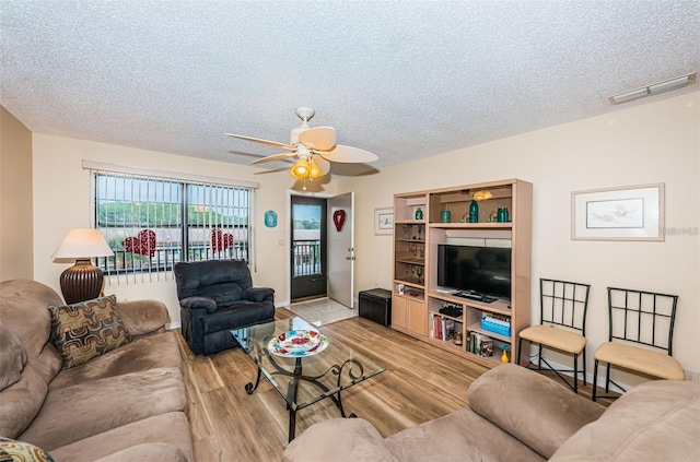 living room with ceiling fan, light wood-type flooring, and a textured ceiling