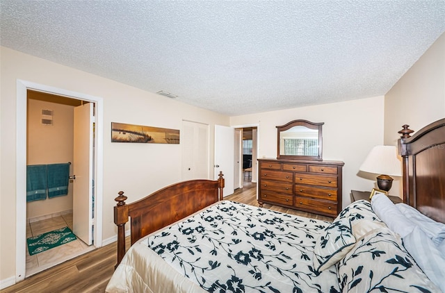 bedroom featuring a closet, dark hardwood / wood-style flooring, ensuite bathroom, and a textured ceiling