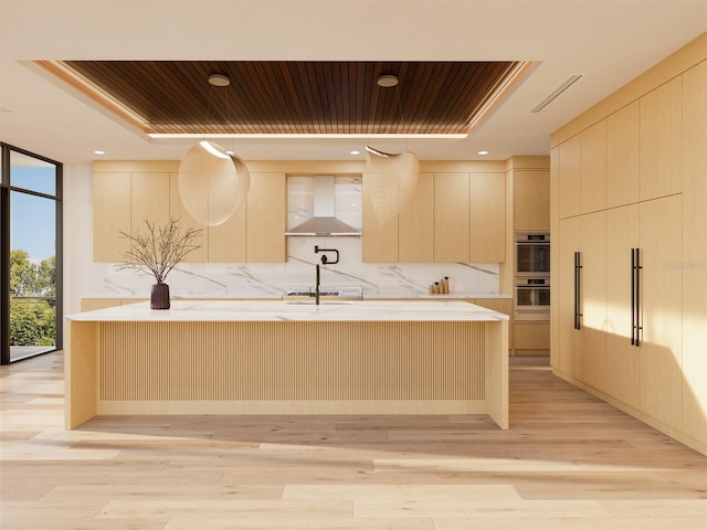 kitchen featuring appliances with stainless steel finishes, light hardwood / wood-style flooring, a wall of windows, and wall chimney range hood