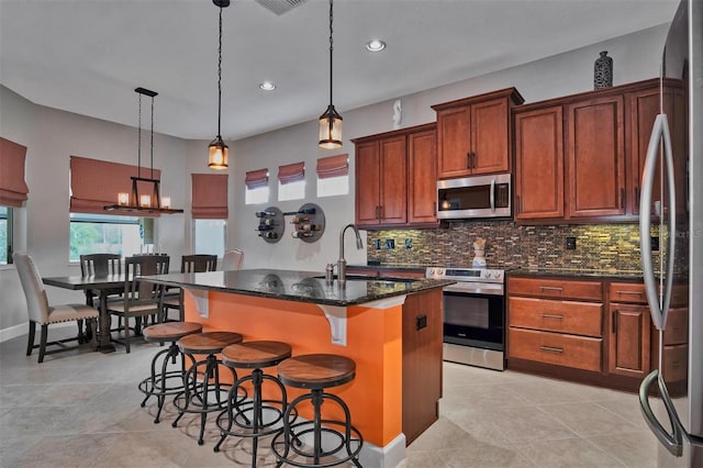 kitchen featuring a kitchen bar, sink, decorative light fixtures, stainless steel appliances, and a center island with sink