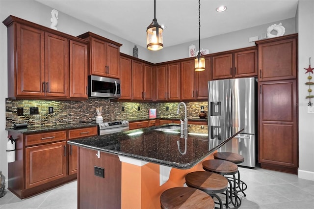 kitchen with hanging light fixtures, appliances with stainless steel finishes, sink, backsplash, and a kitchen island with sink