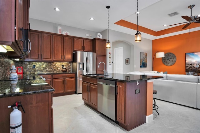 kitchen featuring appliances with stainless steel finishes, tasteful backsplash, hanging light fixtures, a kitchen island with sink, and sink