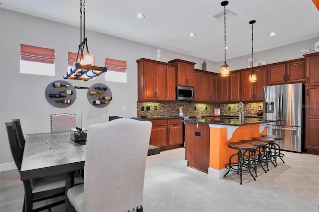 kitchen featuring appliances with stainless steel finishes, decorative light fixtures, a kitchen bar, tasteful backsplash, and a center island with sink