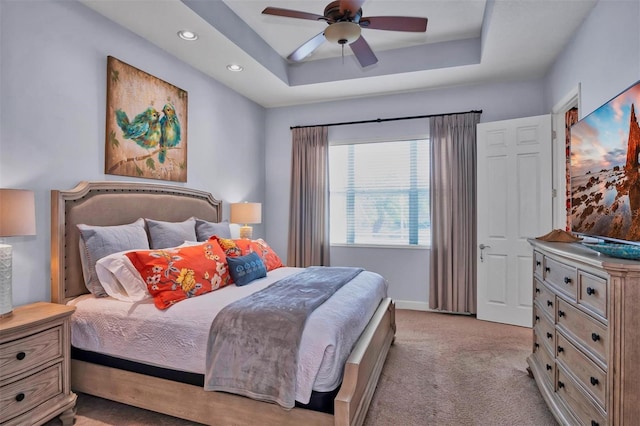 bedroom featuring ceiling fan, a tray ceiling, and light carpet