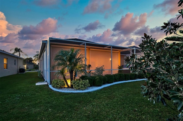 property exterior at dusk with glass enclosure and a yard