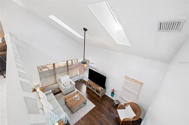 living room featuring ceiling fan, vaulted ceiling with skylight, dark wood-type flooring, and a textured ceiling